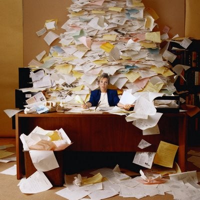 Stock photo of a woman at a desk surrounded by a mound of papers